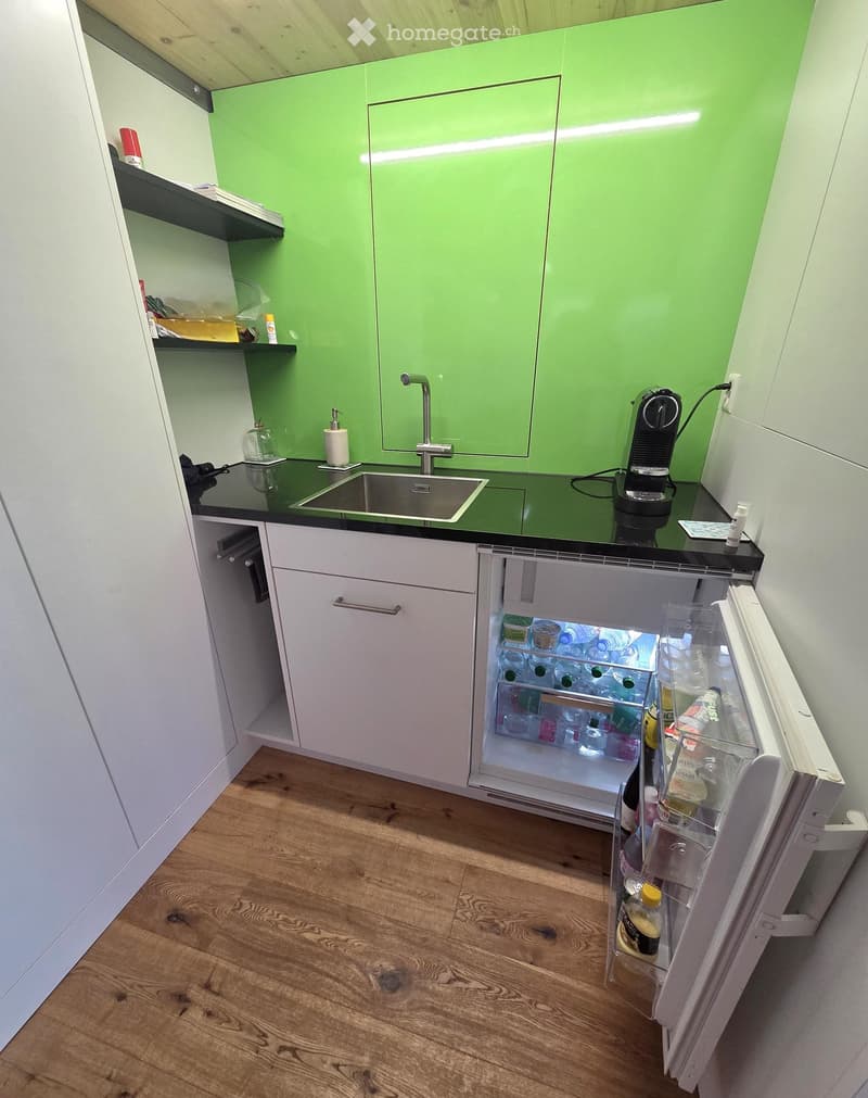 Modern kitchen with green cabinets, white lower cabinets, black countertop, stainless steel sink, and an open refrigerator with drinks inside.