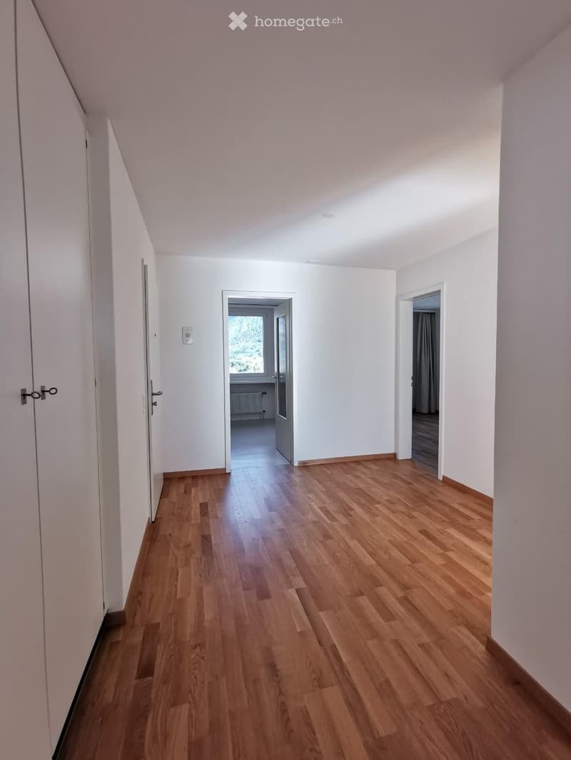 Empty hallway with wooden flooring, white walls, and doors leading to other rooms.