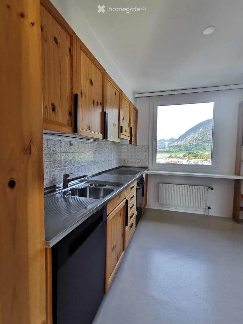 Modern kitchen with wooden cabinets, stainless steel sink, oven, and radiator. Large window offers scenic mountain view.