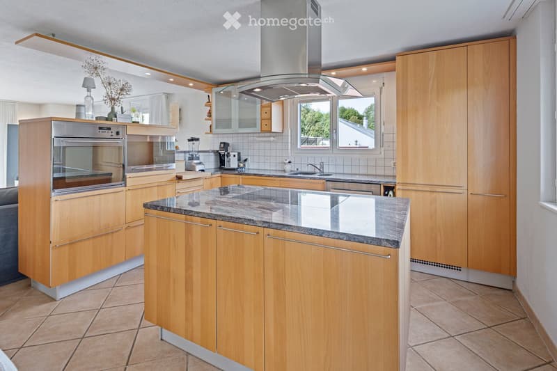 Modern kitchen with light wooden cabinets, granite countertop, stainless steel appliances, and a central island.