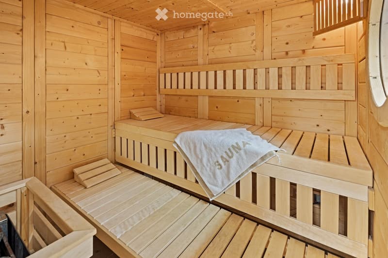Wooden sauna interior with benches and a towel labeled "SAUNA" placed on one of the benches.