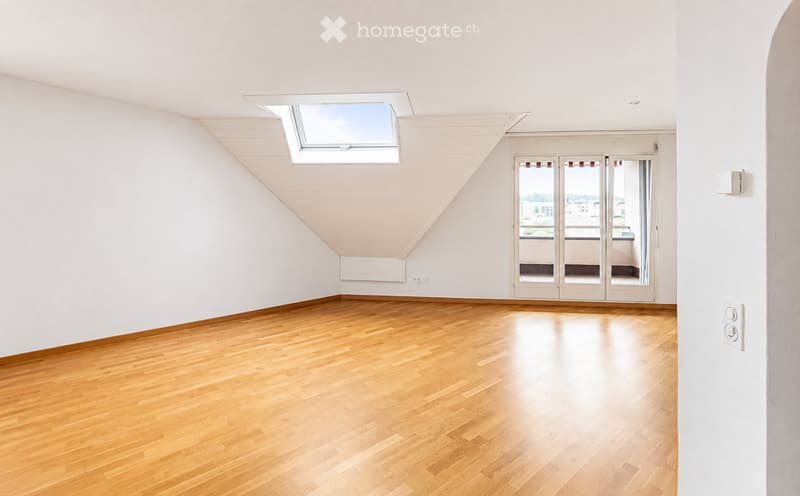 Empty room with wooden flooring, white walls, large skylight, and sliding glass doors leading to a balcony.