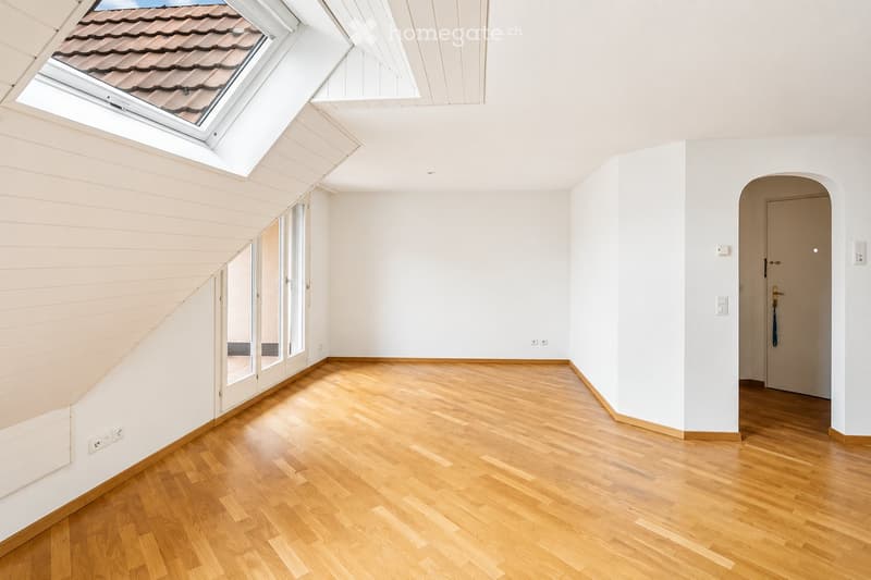 Bright, empty room with wooden flooring, white walls, large skylight, and a door leading to another space.