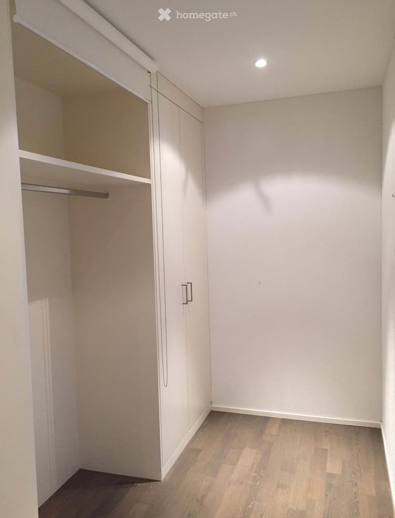 Empty room with white walls, light wooden flooring, and built-in closet with mirrored doors and shelves.