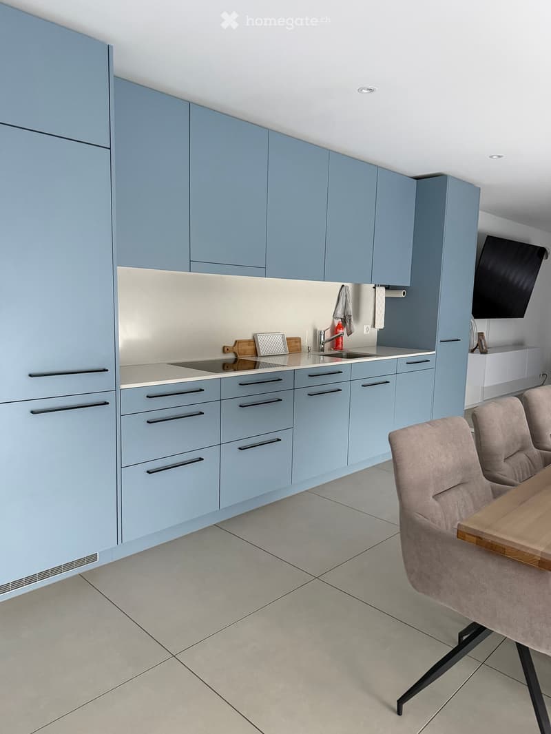 Modern kitchen with light blue cabinets, a sink, and a small dining area with a table and chairs.