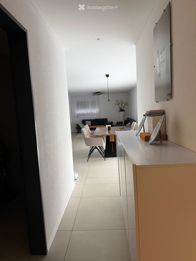 Modern hallway leading to a living area with a sofa, coffee table, and decorative items on a side table.