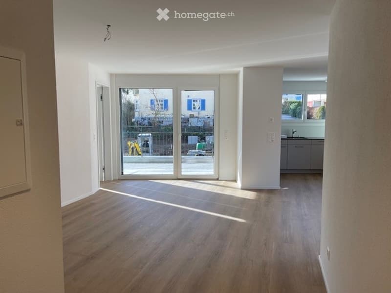 Empty room with wooden flooring, large sliding glass doors leading to a balcony, and a view of the street outside.