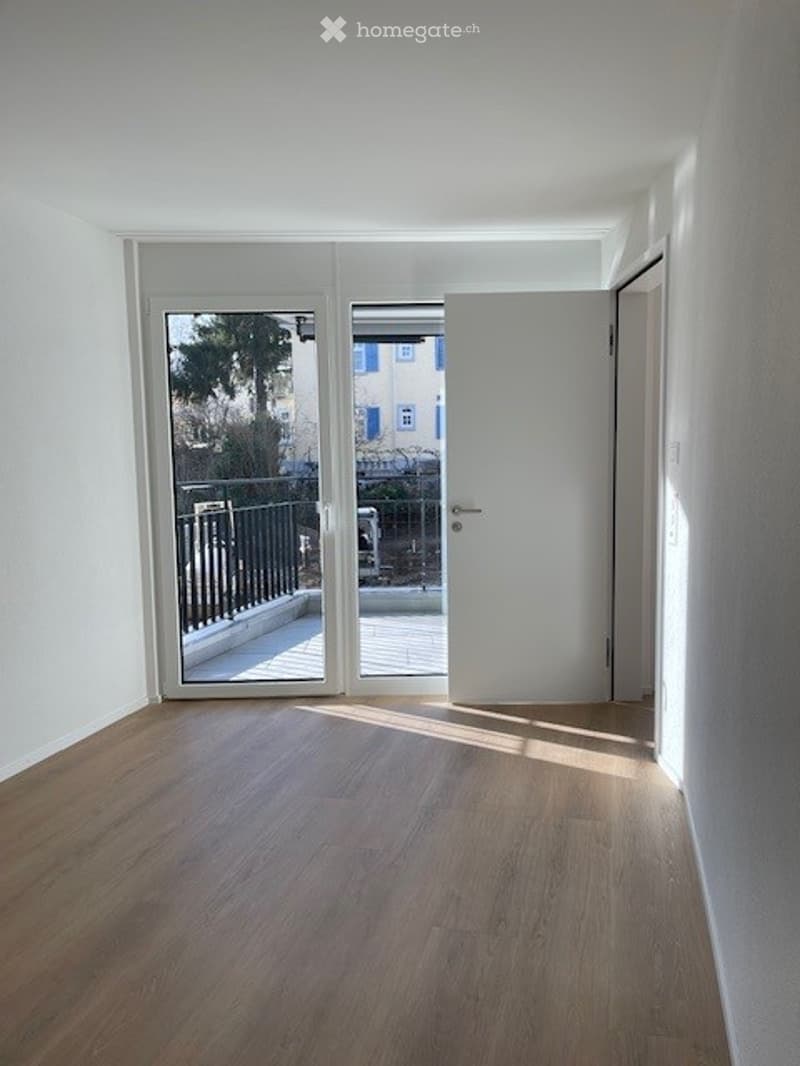 Empty room with wooden flooring, white walls, and a sliding glass door leading to a balcony.