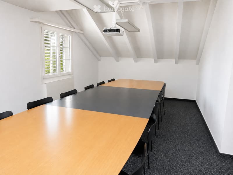 Bright, modern room with a large conference table and chairs, white walls, and a projector mounted on the ceiling.
