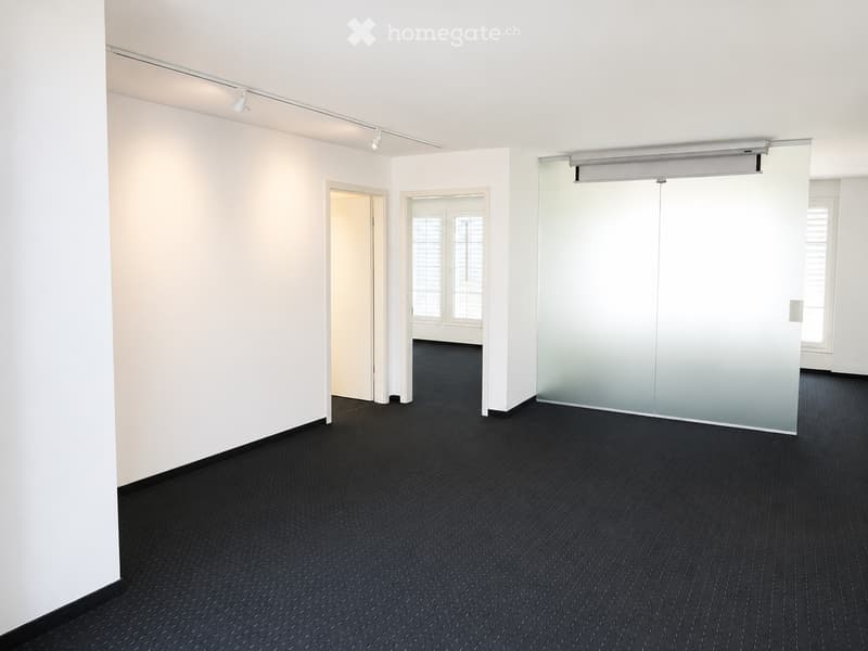 Empty room with white walls, black carpet, and two doors leading to adjacent spaces.