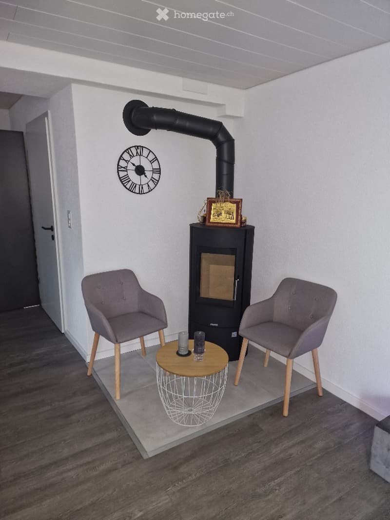 Modern living room with a fireplace, two armchairs, a small round table, and a decorative clock on the wall.