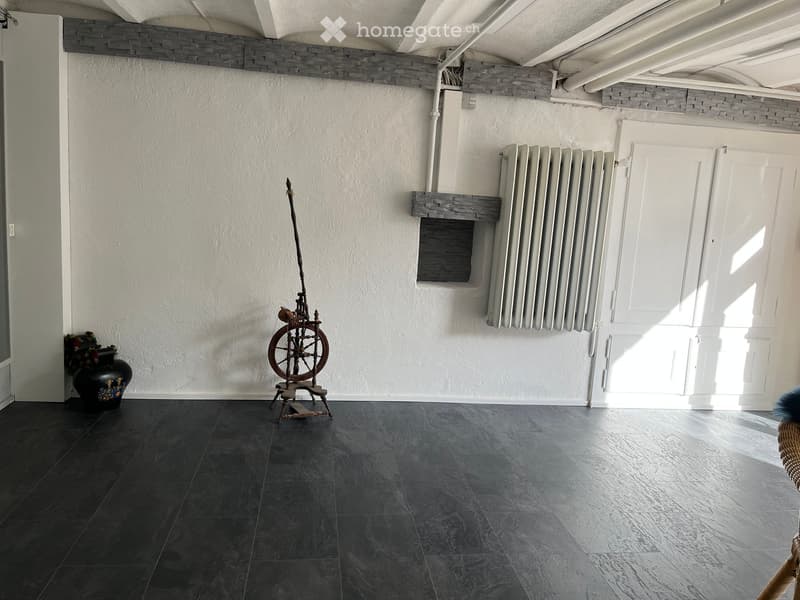 Room with dark tiled floor, white walls, spindle wheel, vase, radiator, and white door.