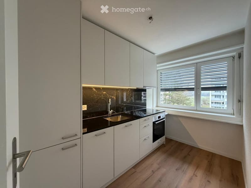 modern kitchen with white cabinets, black countertops, stainless steel sink, oven, window with blinds