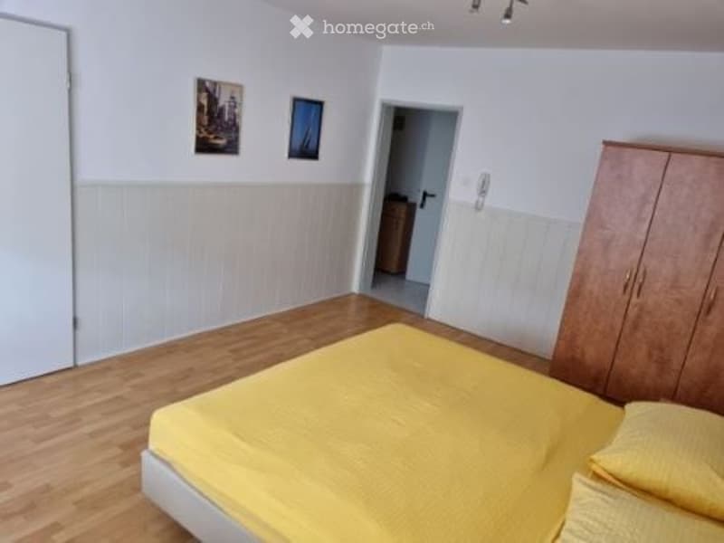 Single bed, wooden floor, wooden wardrobe, wooden headboard, white walls, door, paintings