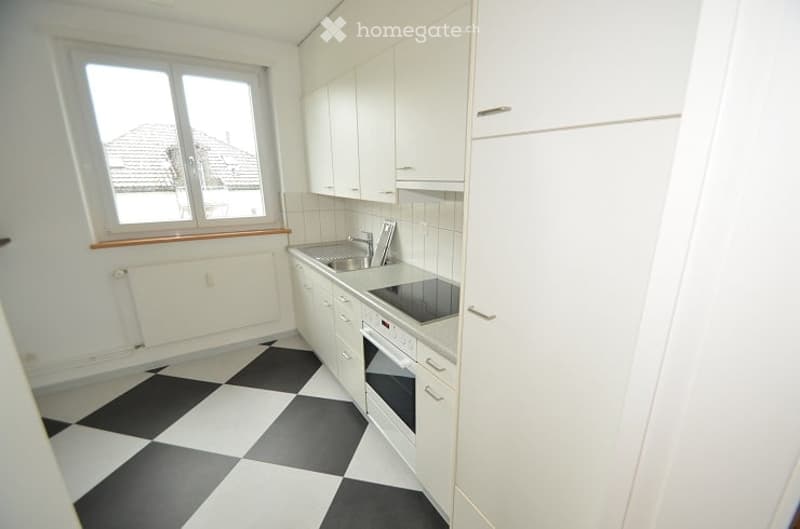 Modern kitchen with white cabinets, black and white checkered floor, stainless steel sink, and built-in oven.