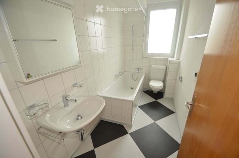 Modern bathroom with white tiles, black and white checkered floor, sink, bathtub, toilet, and mirror.