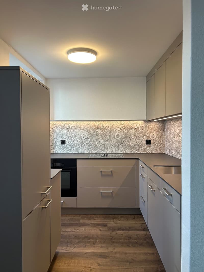 Modern kitchen with light-colored cabinets, wooden flooring, and a decorative backsplash.