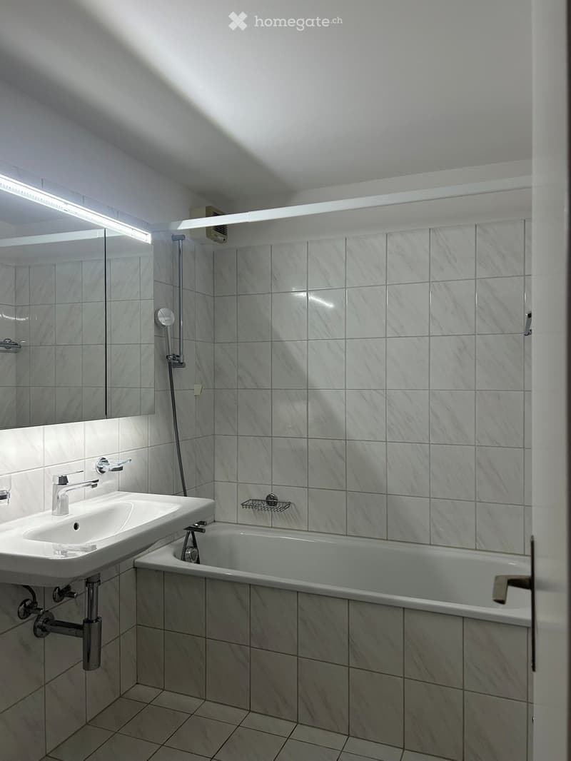 Modern bathroom with white tiles, a sink, a bathtub, a mirror, and a shower head.