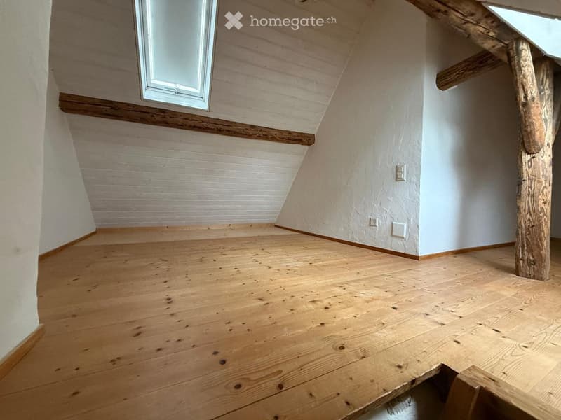 Empty attic space with wooden flooring, white walls, and exposed wooden beams. Features a skylight window and electrical outlets on the wall.