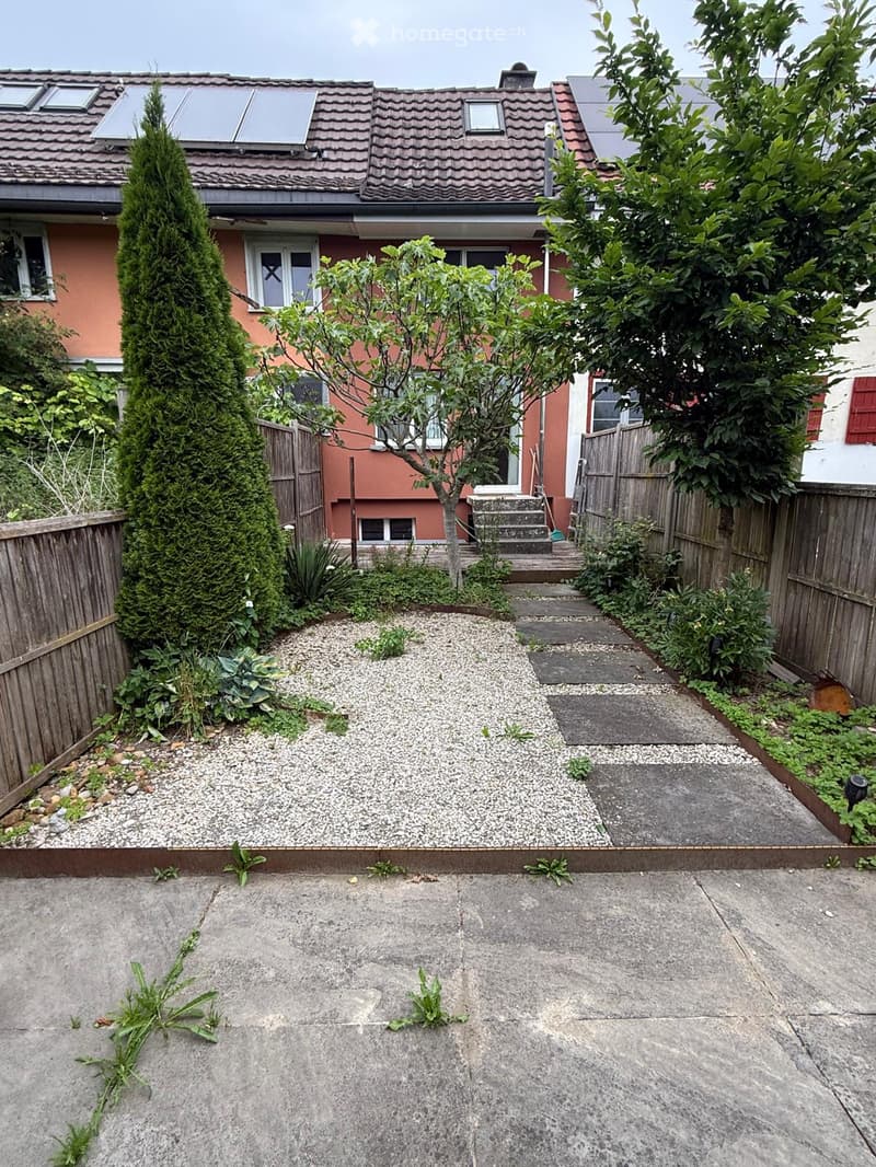 Garden area with gravel, concrete patio, wooden fence, and steps leading to a house entrance.