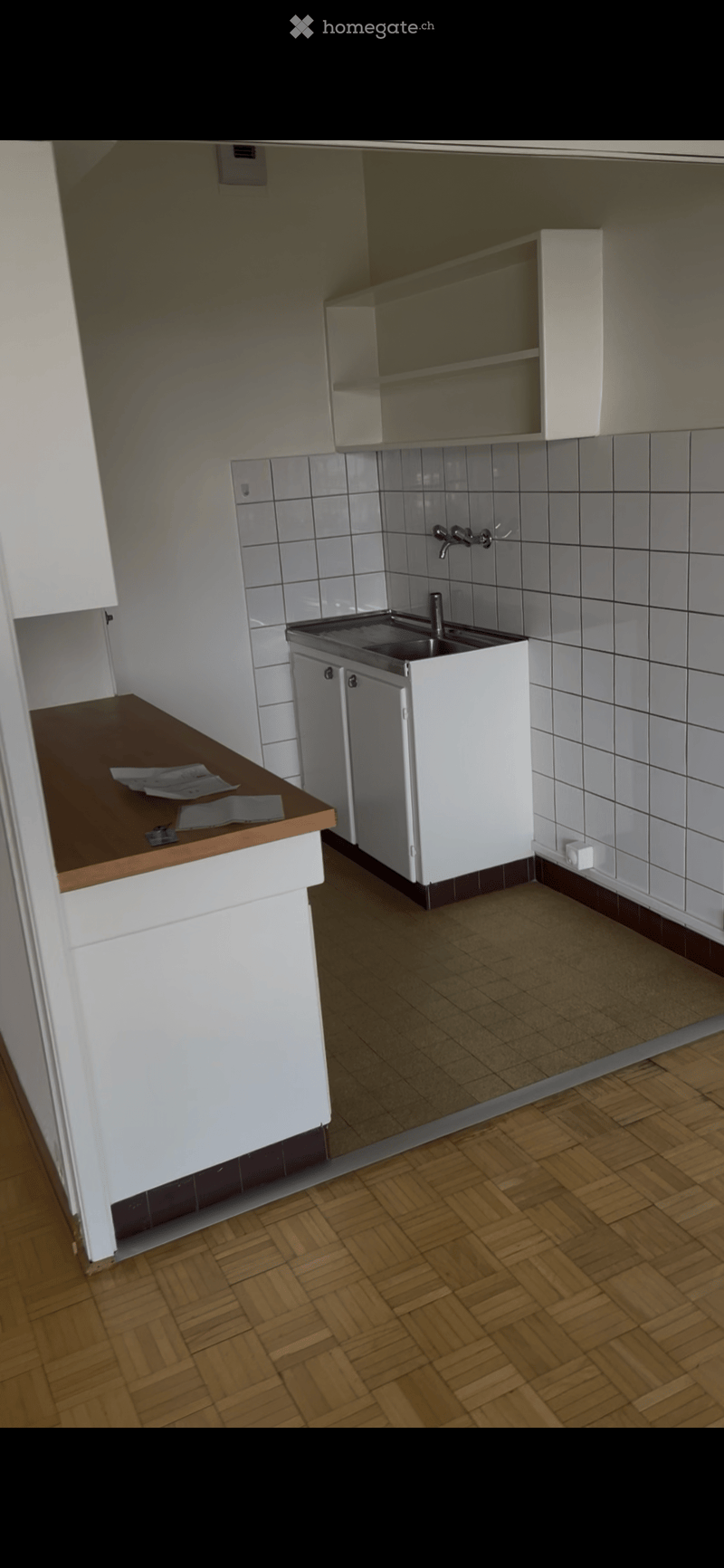 Modern kitchen with white cabinets, a stainless steel sink, and a wooden countertop. The floor is made of parquet, and the walls are tiled.