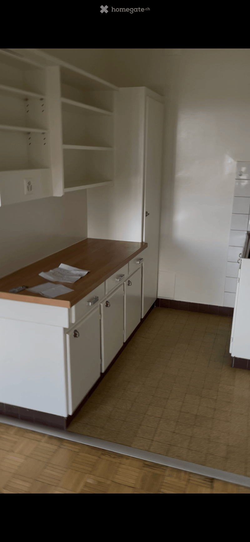 Empty kitchen with white cabinets, wooden countertop, and tiled floor. No appliances or furniture present.