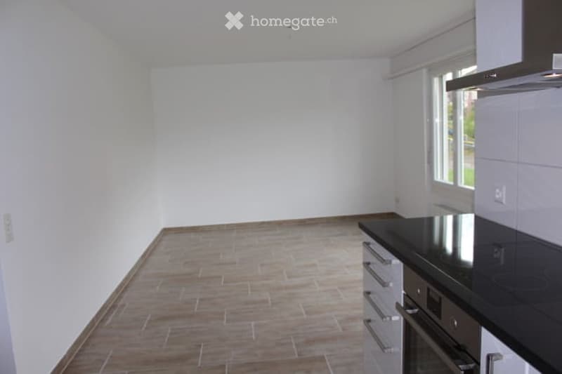 Empty kitchen with white walls, wooden floor, and black countertop. No furniture or appliances visible.
