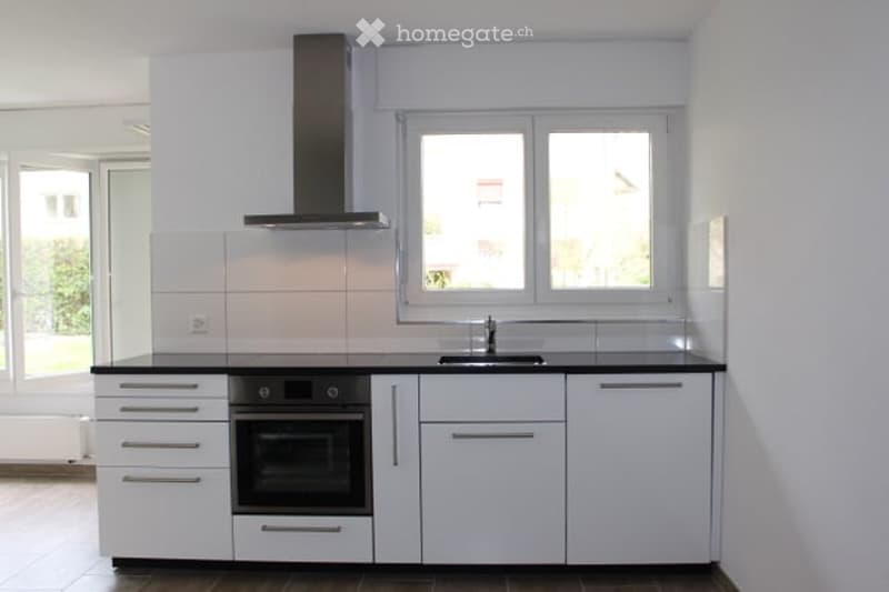 Modern kitchen with white cabinets, black countertops, built-in oven, and stainless steel sink.