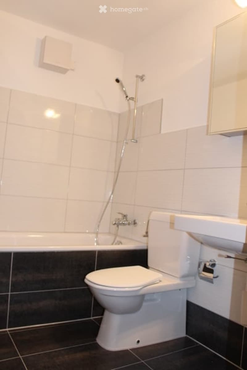 Modern bathroom with white tiles, a bathtub, toilet, sink, and a shower fixture.