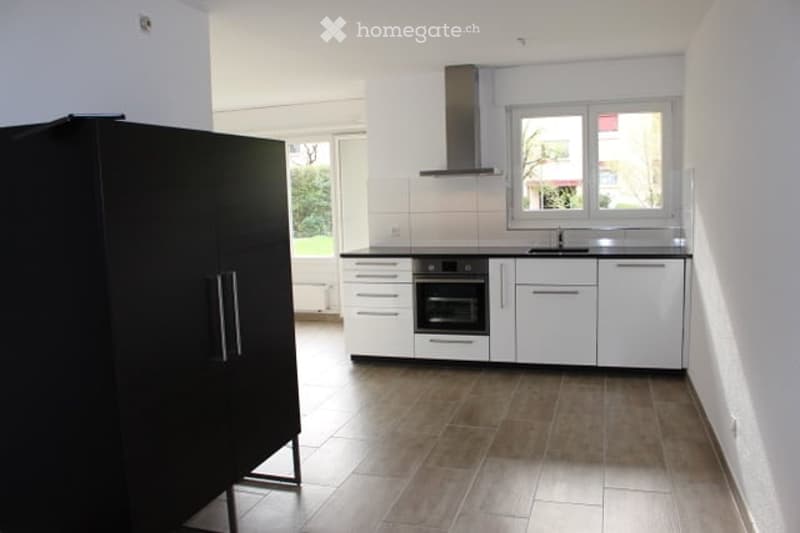 Modern kitchen with white cabinets, black countertops, and a built-in oven. Features a range hood, sink, and faucet, with a large window providing natural light.