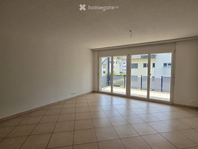Empty room with tiled floor, large sliding glass doors leading to a balcony, and white walls.