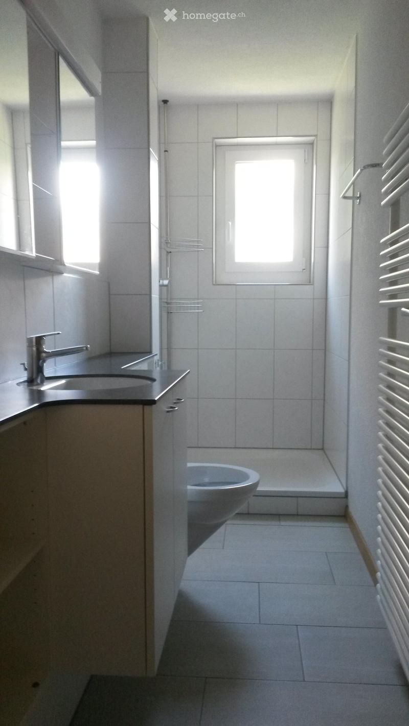 Modern bathroom with white tiles, a sink with a chrome faucet, a toilet, and a radiator on the wall.