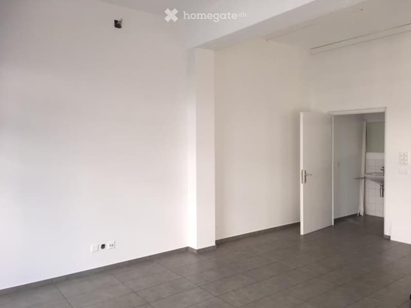 Empty room with white walls and dark tiled floor, featuring an open doorway leading to another room.