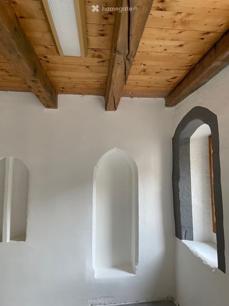 Empty room with white walls, wooden ceiling beams, and arched niches in the wall.