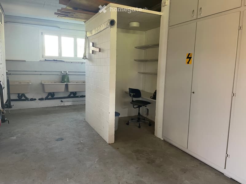 Empty room with concrete floor, white tiled wall, built-in sink area, and a small office area with a chair and shelves.