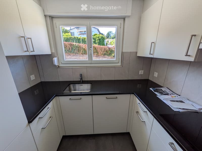 Modern kitchen with white cabinets, dark countertops, and a stainless steel sink. Papers are placed on the counter.