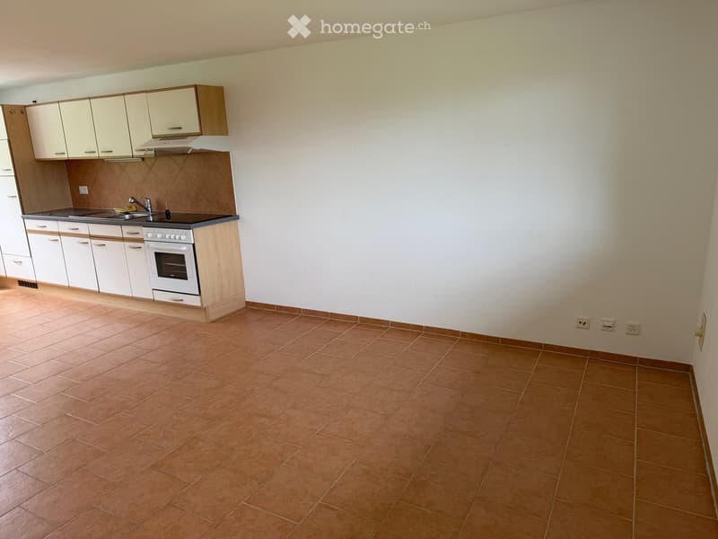 Empty kitchen with white cabinets, a sink, a faucet, and an oven. Brown tiled floor and white walls.