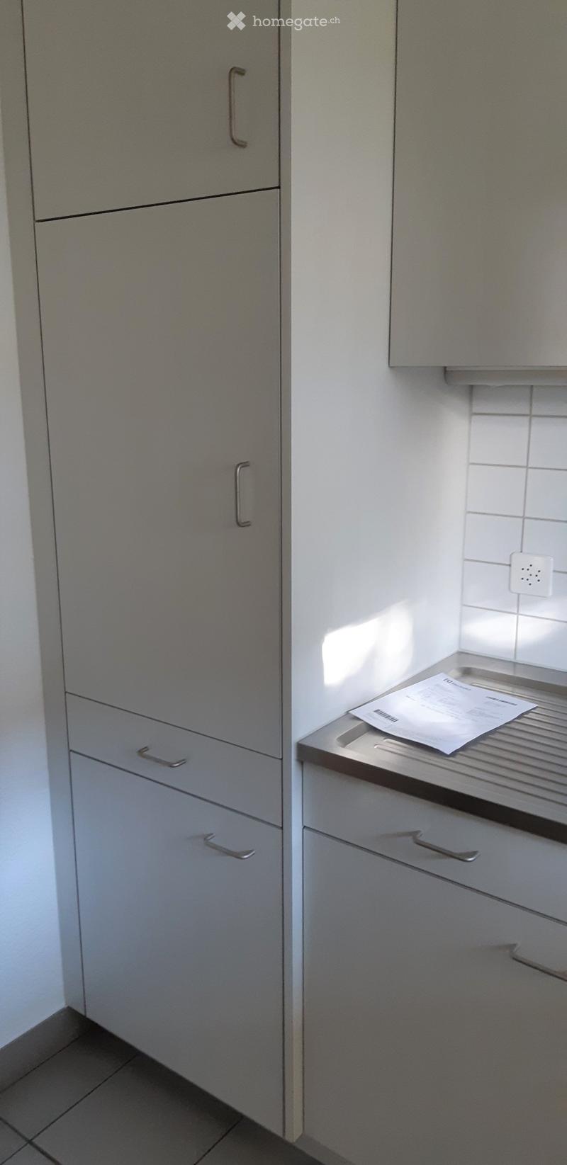 Empty room with grey cabinets, tiled wall, and a small countertop with a paper on it.