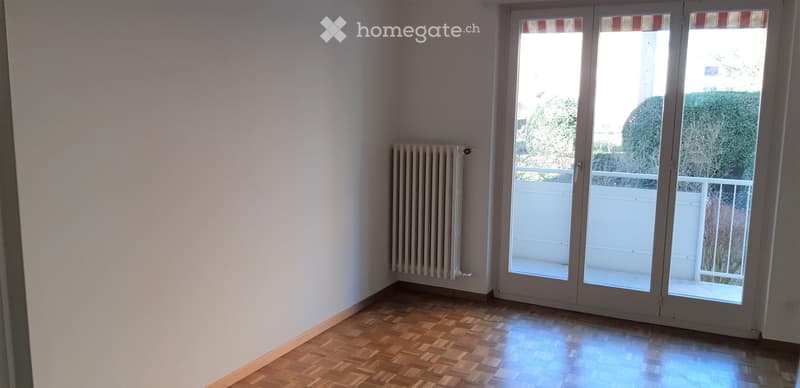 Empty room with wooden flooring, white walls, radiator, and large sliding glass doors leading to a balcony.
