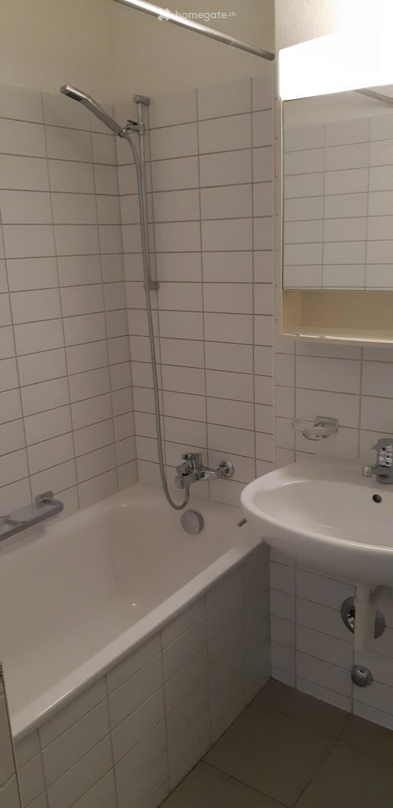 Bathroom with a bathtub, sink, and showerhead. The walls are tiled with light-colored tiles, and the floor is also tiled.