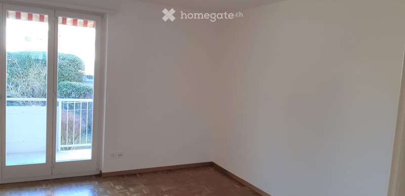 Empty room with wooden flooring, white walls, and a sliding glass door leading to a balcony.