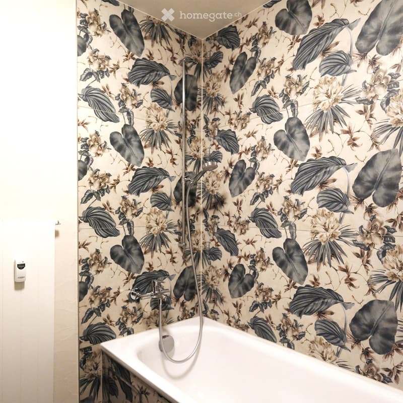 Bathtub with floral patterned wallpaper featuring large leaves and flowers, modern faucet and showerhead.