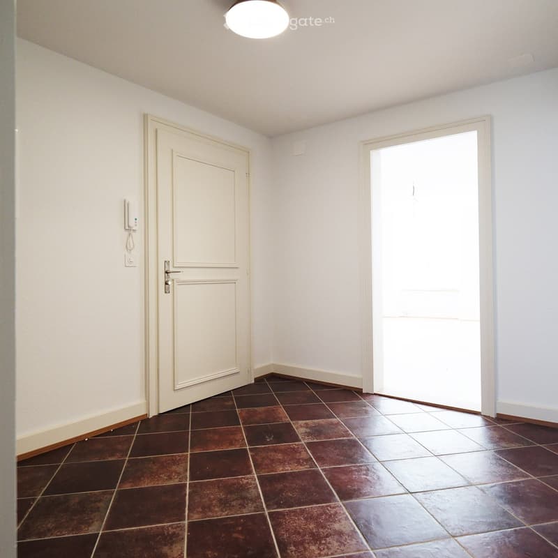 Empty hallway with brown tiled floor, white walls, and a closed door on one side and an open door on the other.