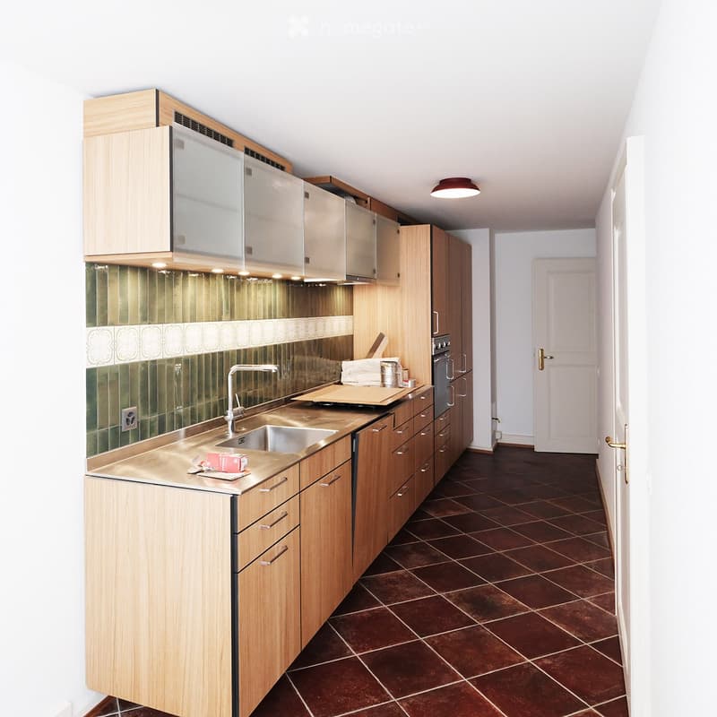 Modern kitchen with wooden cabinets, stainless steel sink, and brown tiled floor.