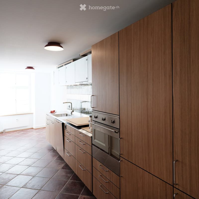 Modern kitchen with wooden cabinets, stainless steel oven, sink, and light fixtures.