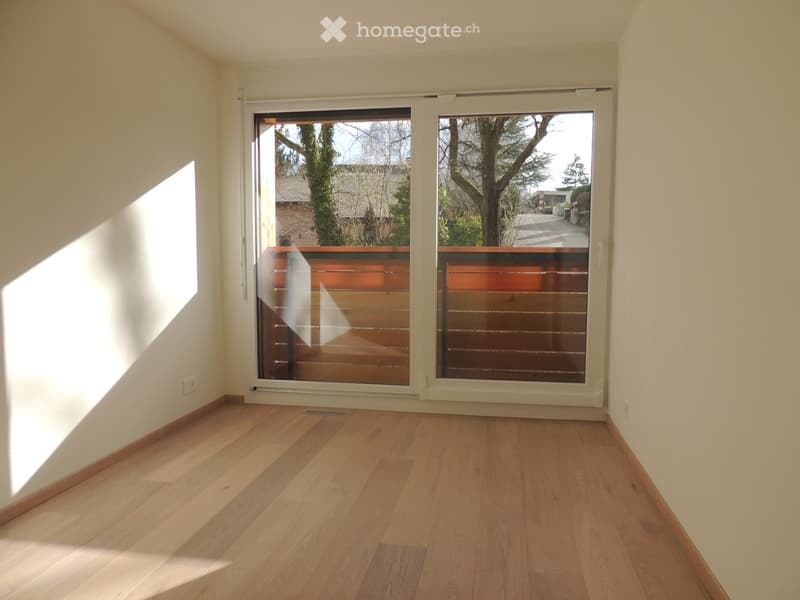 Empty room with wooden flooring, large sliding glass doors leading to a balcony, and natural light streaming in.