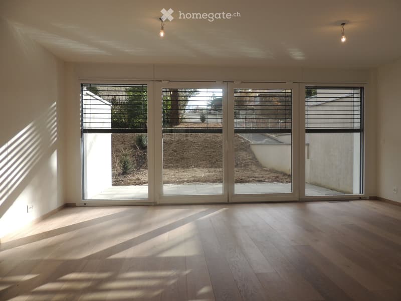 Empty room with wooden flooring, large sliding glass doors, and natural light streaming in.
