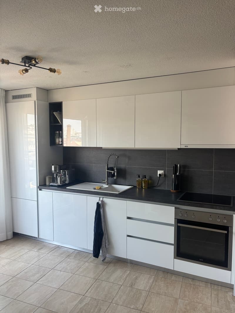 Modern kitchen with white cabinets, stainless steel appliances, and a black countertop. Features include a sink, faucet, oven, coffee maker, and various kitchen items.