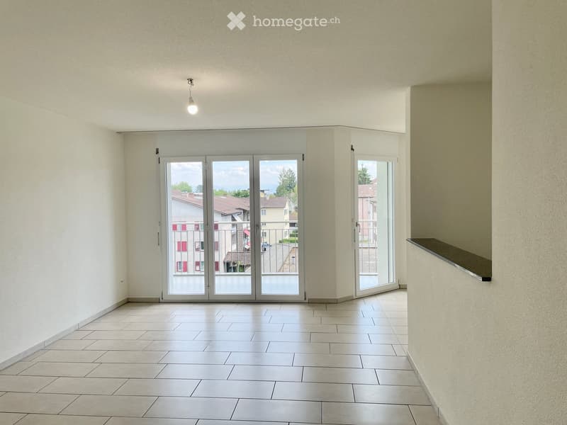 Empty room with tiled floor, white walls, large sliding glass doors leading to a balcony, and a single light fixture on the ceiling.