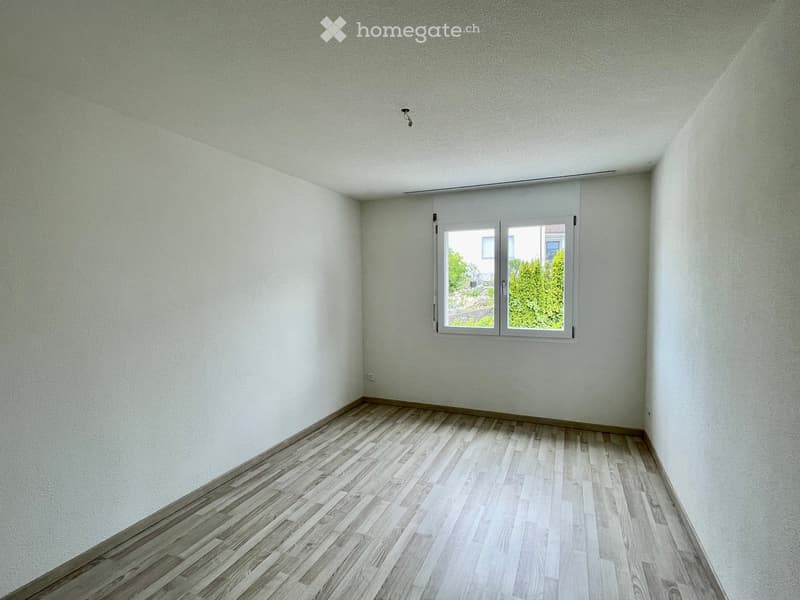 Empty room with light grey walls, wooden flooring, and a single window with white frame and blinds.